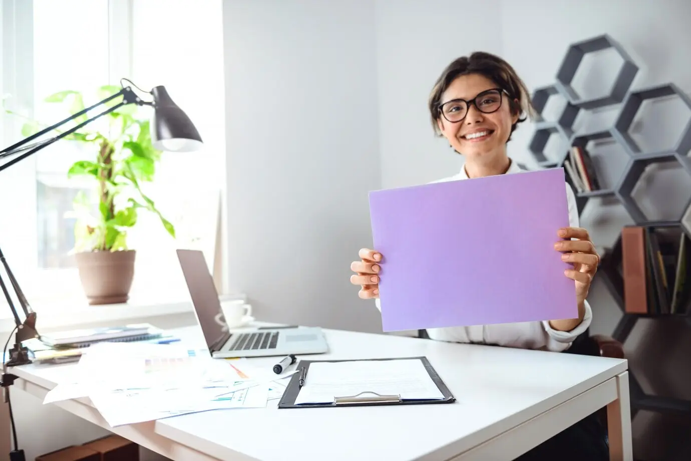 Junge, schöne, fröhliche Geschäftsfrau lächelt und hält Papier am Arbeitsplatz im Büro.
