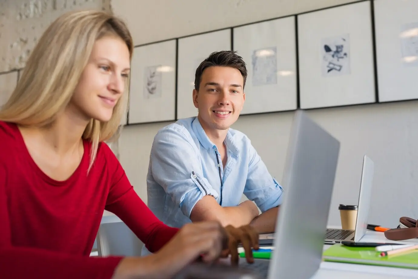 Online tätige Remote-Beschäftigte: ein junger Mann und eine junge Frau arbeiten an einem Laptop in einem Open-Space-Coworking-Büroraum.
